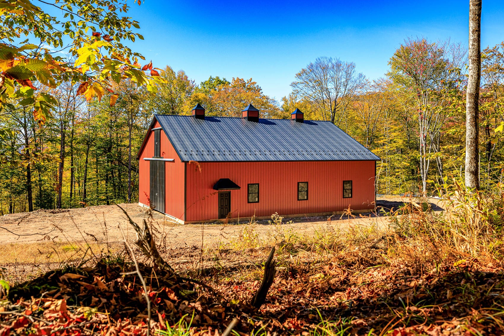 Red custom barn framed by woodland and autumn leaves