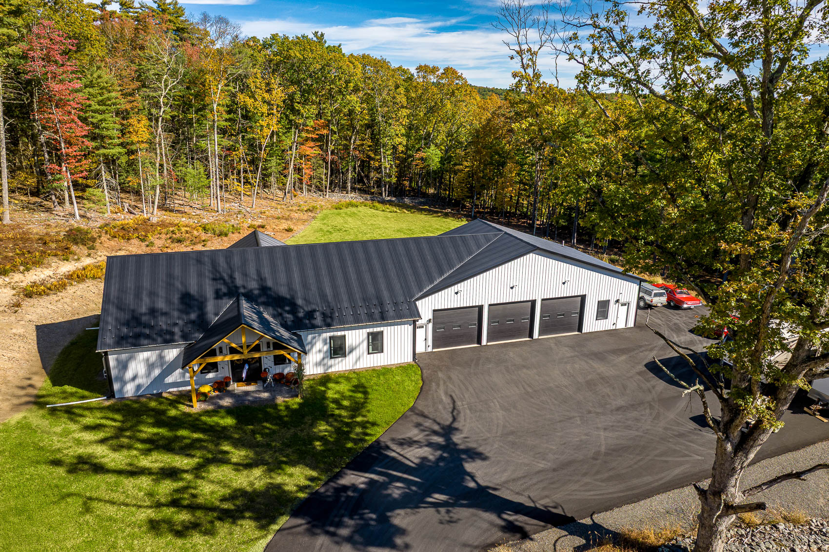 Aerial view of a white pole building with a paved drive and wooded acreage